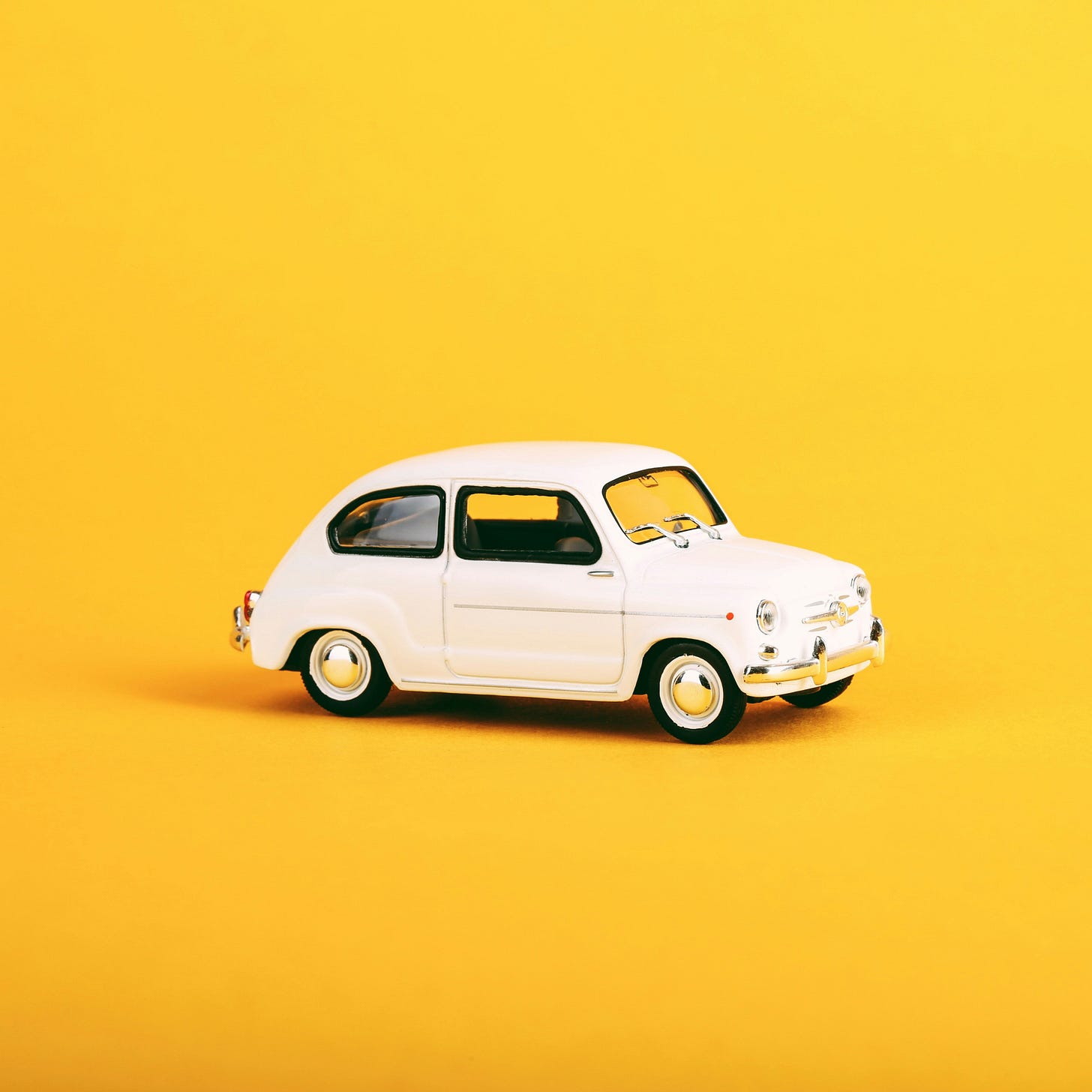 A white Volkswagen car model against a sunny yellow background.