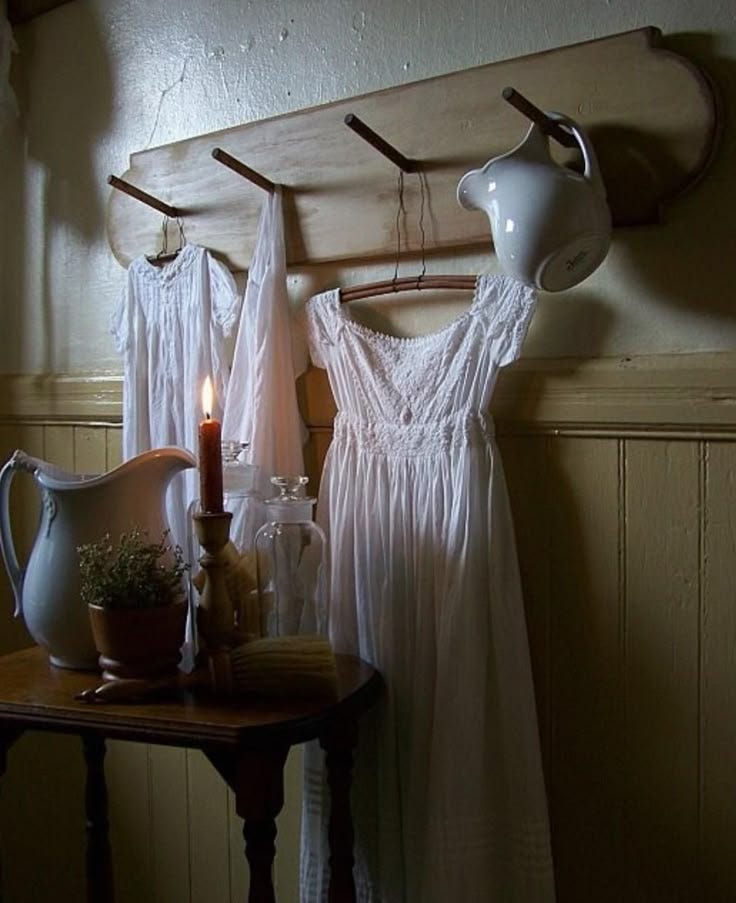 This may contain: two white dresses hanging on a wall next to a table with a candle and potted plant