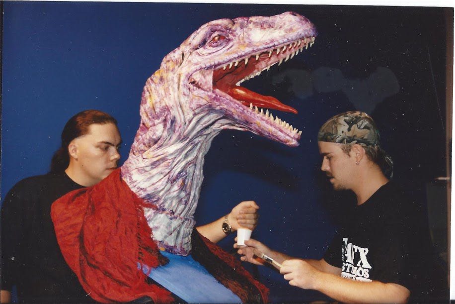 A purple raptor puppet head, its mouth open in a roar.