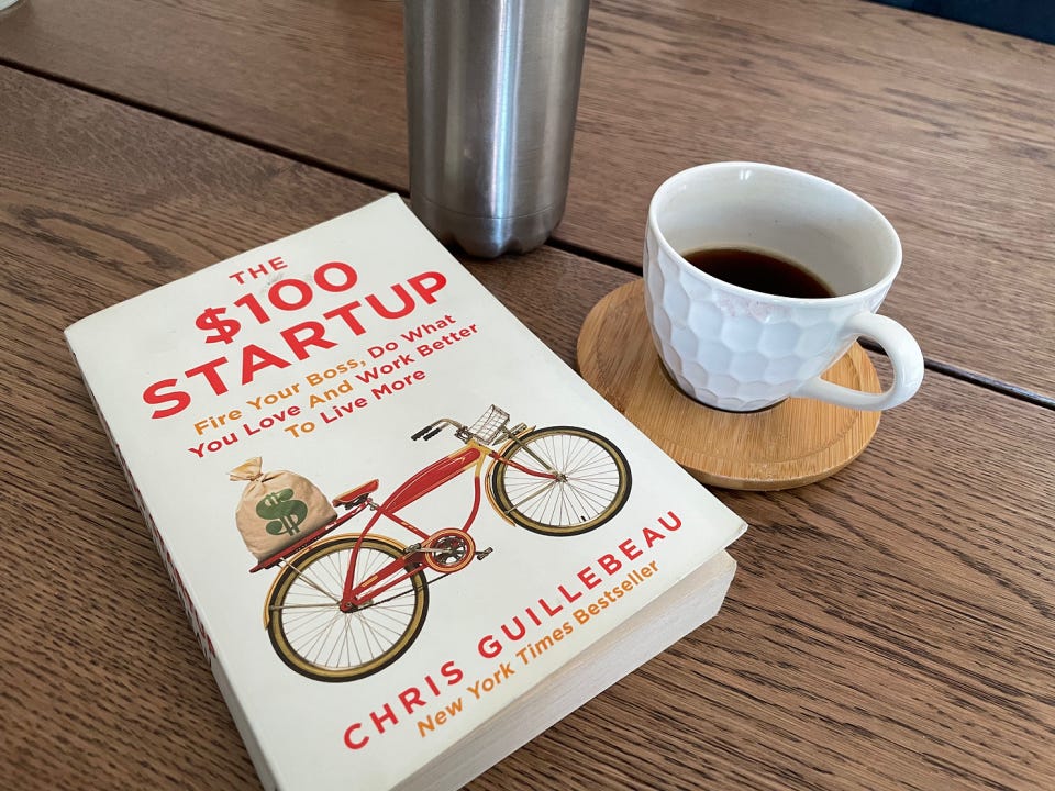 This image shows the book The $100 Startup by Chris Guillebeau, placed beside a cup of coffee on a wooden table, symbolizing work freedom. This image shows the book The $100 Startup by Chris Guillebeau, placed beside a cup of coffee on a wooden table, symbolizing work freedom.