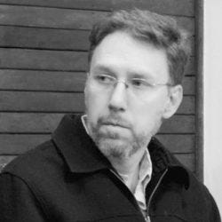 20240306_andre_frazao_helene Homem de cabelos castanhos claros e barba branca Ele usa camisa e casaco e óculos de armação quadrada e preta