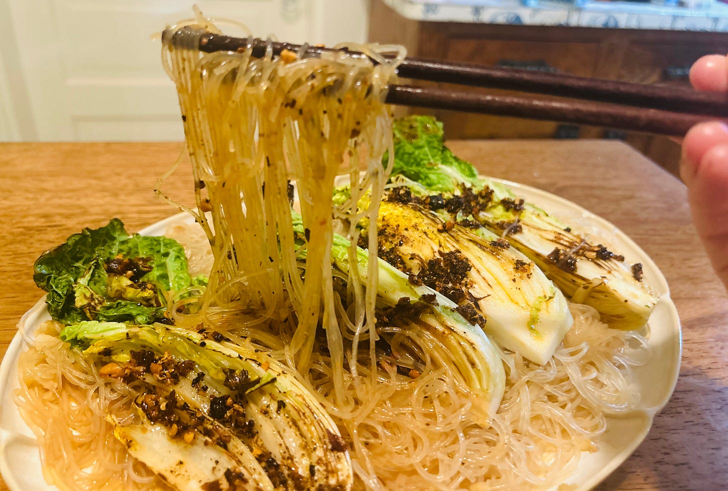 Chopsticks are pulling noodles up from the cabbage and noodle dish.