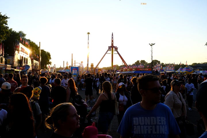 Overhead shot of attendees, friends in the gondola behind me on the Skyride, seed art wall at the Crop Art show, attendee looking over loaves of bread, amusement rides, golden hour behind the crowd, Sweet Martha's Cookies at night.