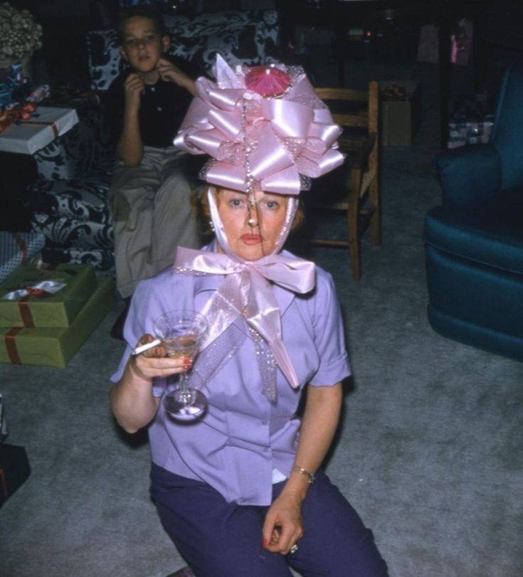 This may contain: a woman sitting on the floor with a glass in her hand and wearing a pink hat