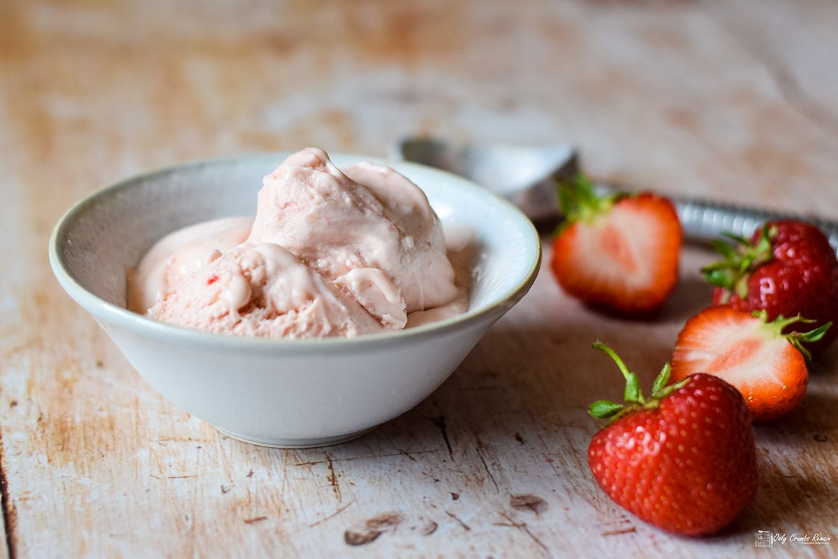 bowl of strawberry ice cream with fresh strawberries on the side.