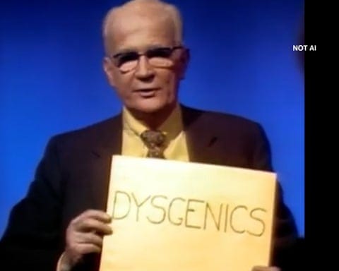 Shot from a TV show in the past, with a man in glasses wearing a suit and a yellow shirt holding a sign that reads 'Dysgenics' in front of a blue screen
