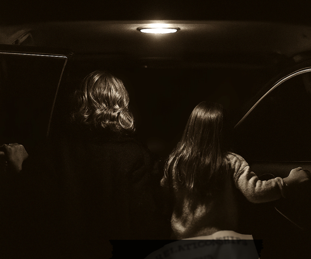 Back of mother & daughter in a dark car with the dome light on