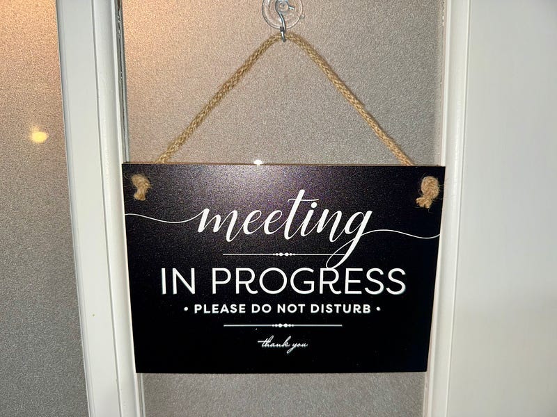A black meeting in progress sign on a white door