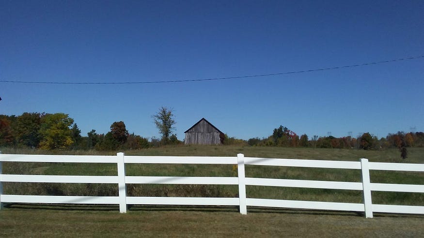 A rustic barn and a white painted fence on a sunny fall day in Cooper, Ontario.