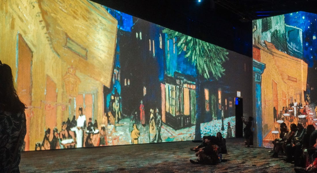 A wall with Van Gogh paintings on it and people sitting on benches nearby A wall with Van Gogh paintings on it and people sitting on benches nearby
