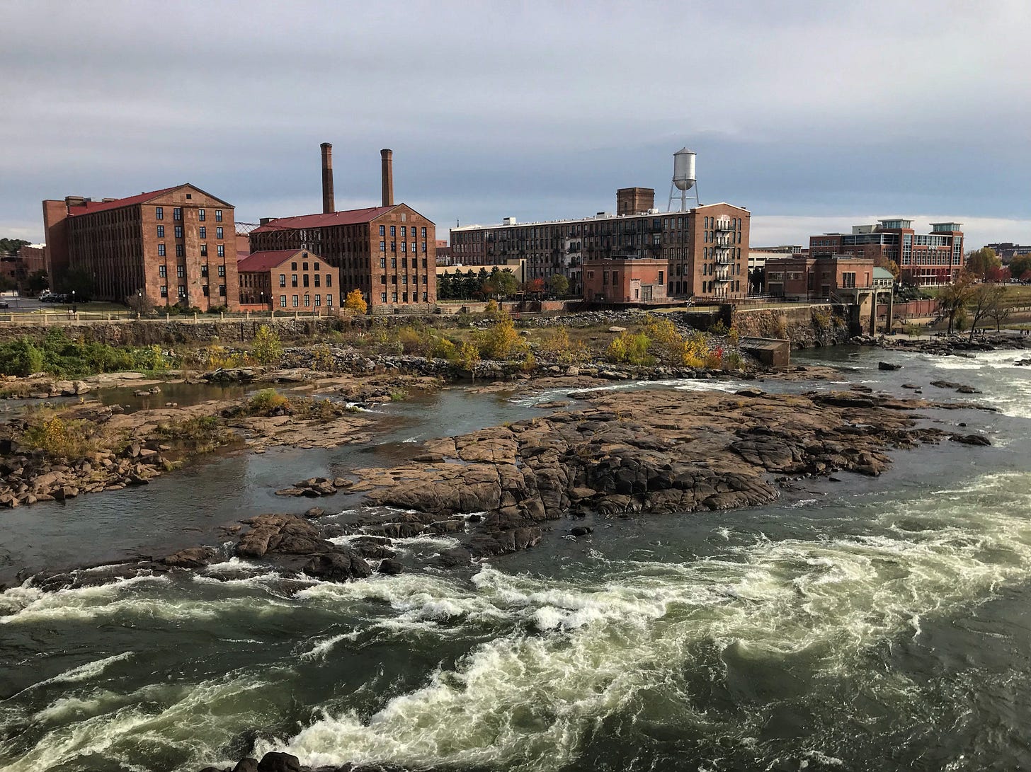A view of Columbus, Ga along the Chattahoochee River, showing red brick buildings and white water.