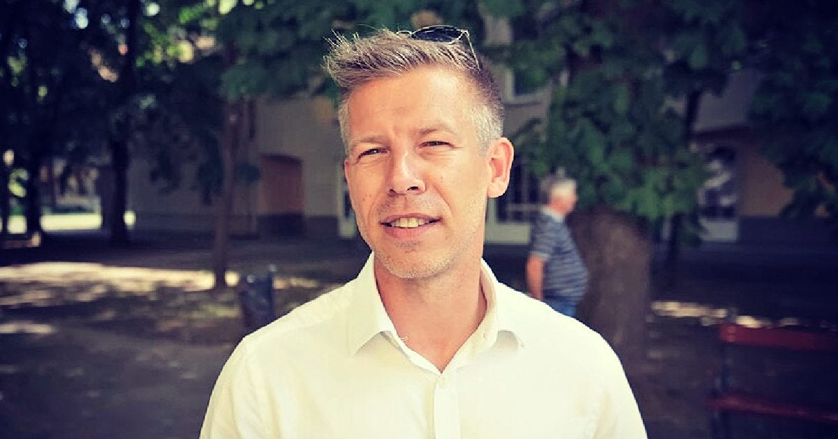 Smiling man in a white shirt stands outdoors with trees in the background, showcasing a relaxed atmosphere. Smiling man in a white shirt stands outdoors with trees in the background, showcasing a relaxed atmosphere.
