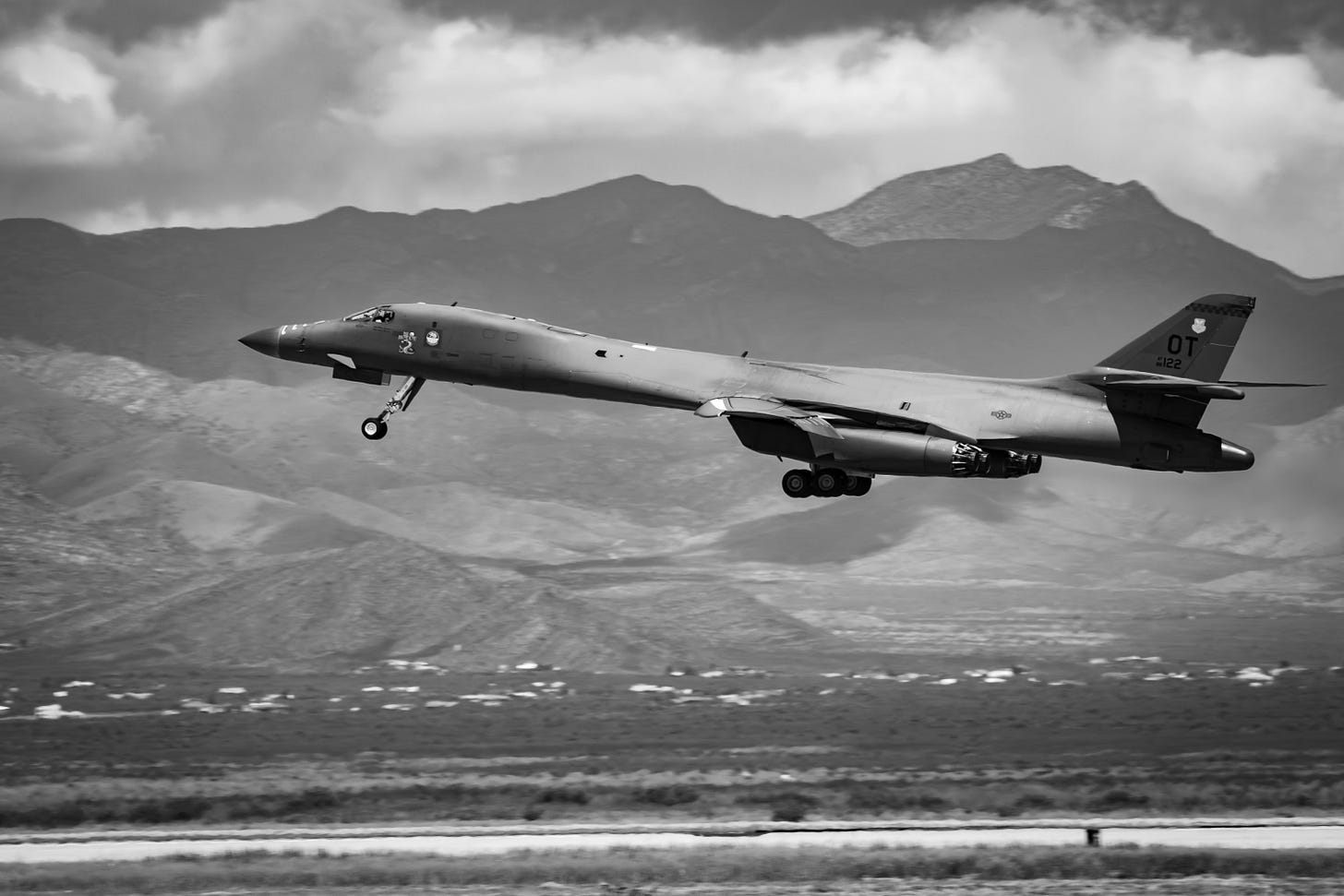 Black & White image of a B-1 aircraft taking off with mountains and cumulus clouds in the background Black & White image of a B-1 aircraft taking off with mountains and cumulus clouds in the background