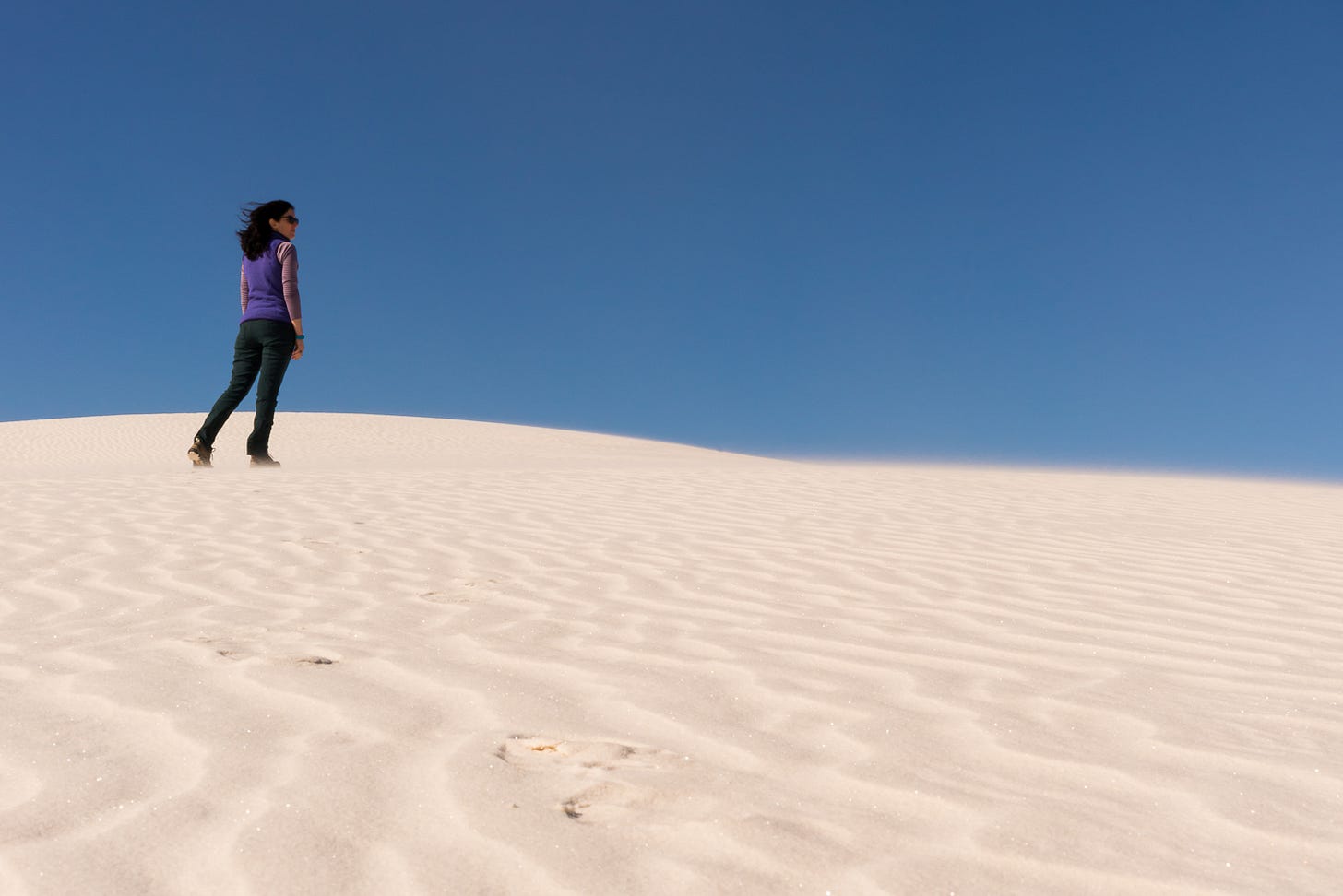 A woman walking on a sand dune.