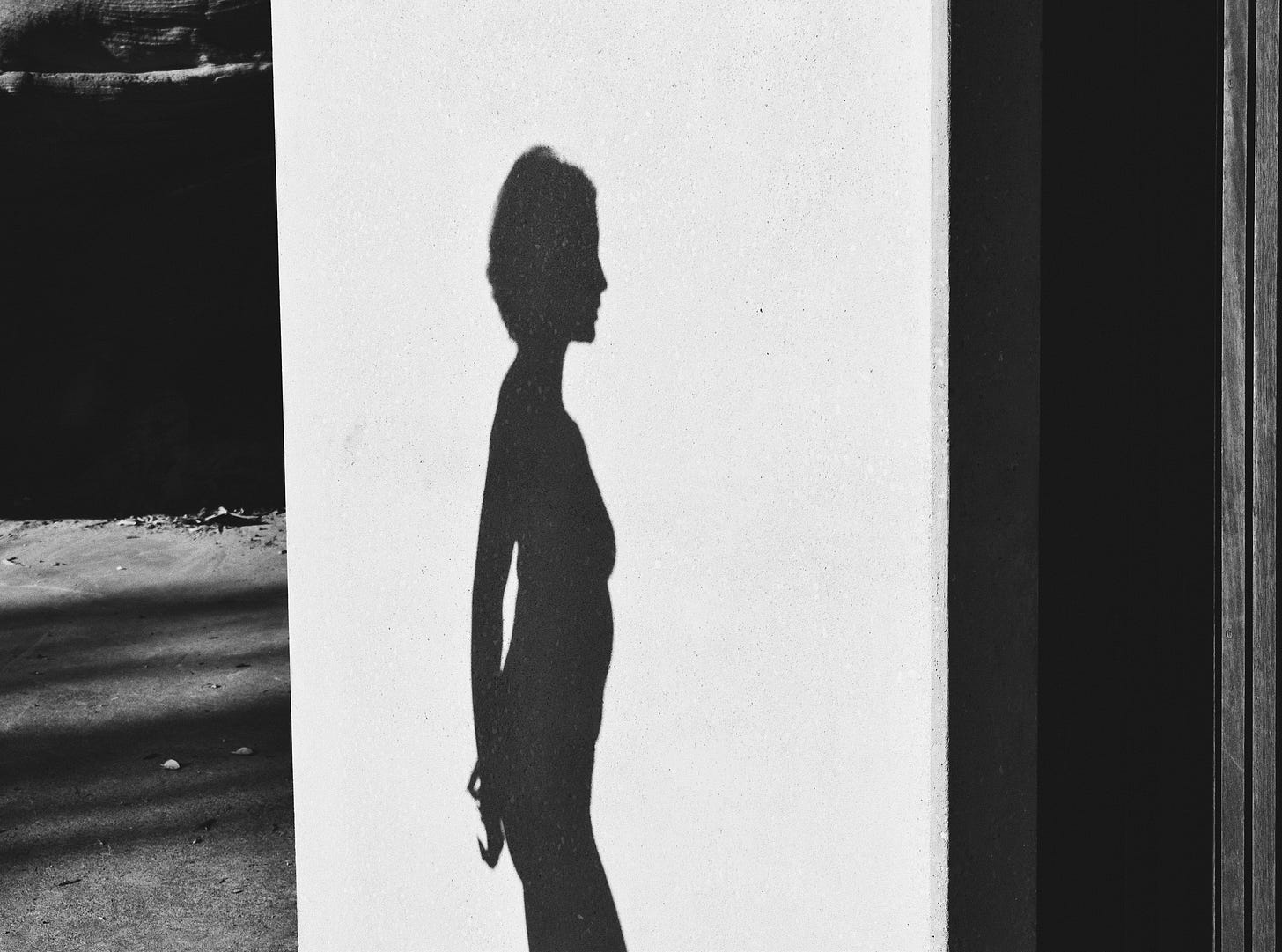 Shadow silhouette of a lean woman's profile can be seen on a white wall.