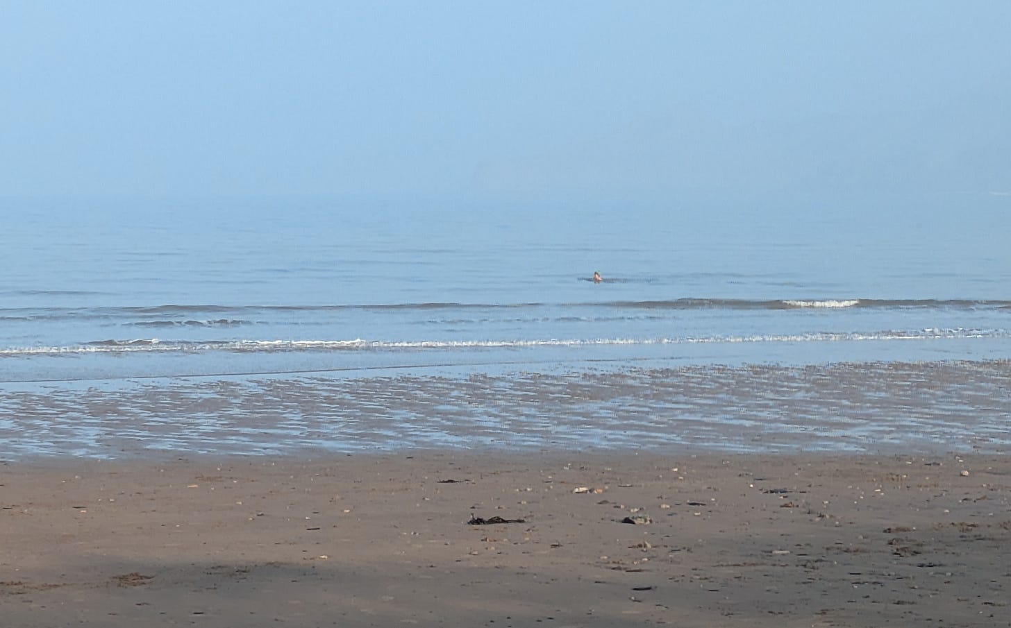 A view of the sea with a small swimmer's head just visible, wearing a green wooly hat