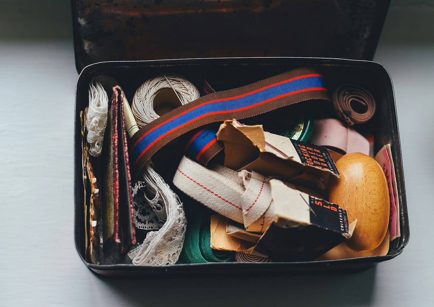 Color photo of a metal tin containing an assortment of string, cord, lace, and other sewing doo-dads
