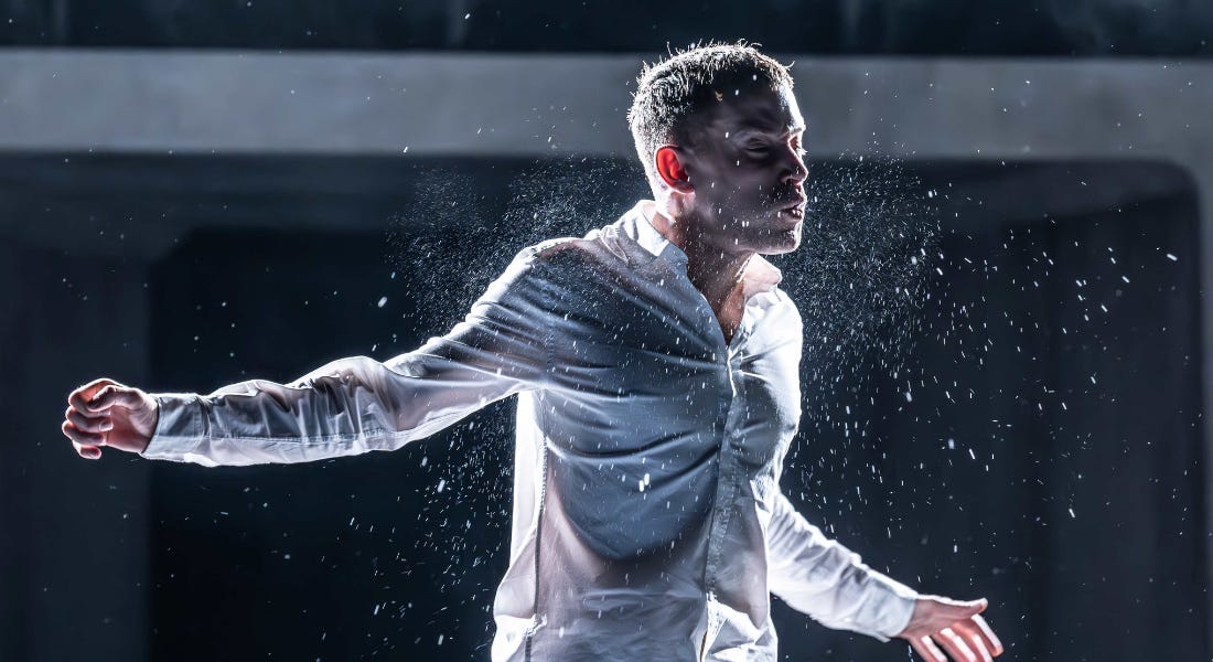 A man wearing a white shirt with spittle drops around him, on a stage with a dark background