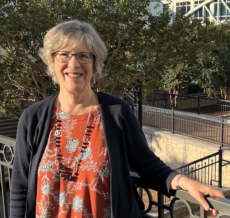Woman with glasses and orange flowered top, black cardigan and silver necklace