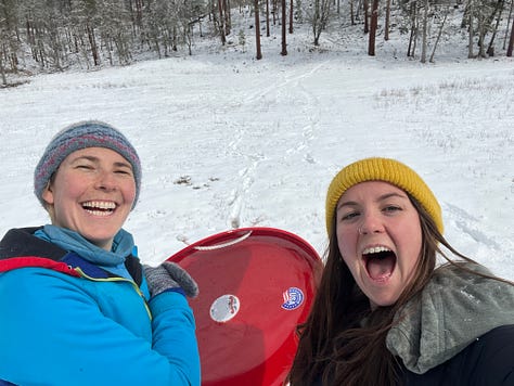 Main lodge covered in snow; inside the yoga yurt; partner yoga; cabin interior; the group, enjoying dinner; a bunch of smiling yoga friends; two friends on a bridge; two friends enjoying sledding; Buckhorn Springs welcome sign