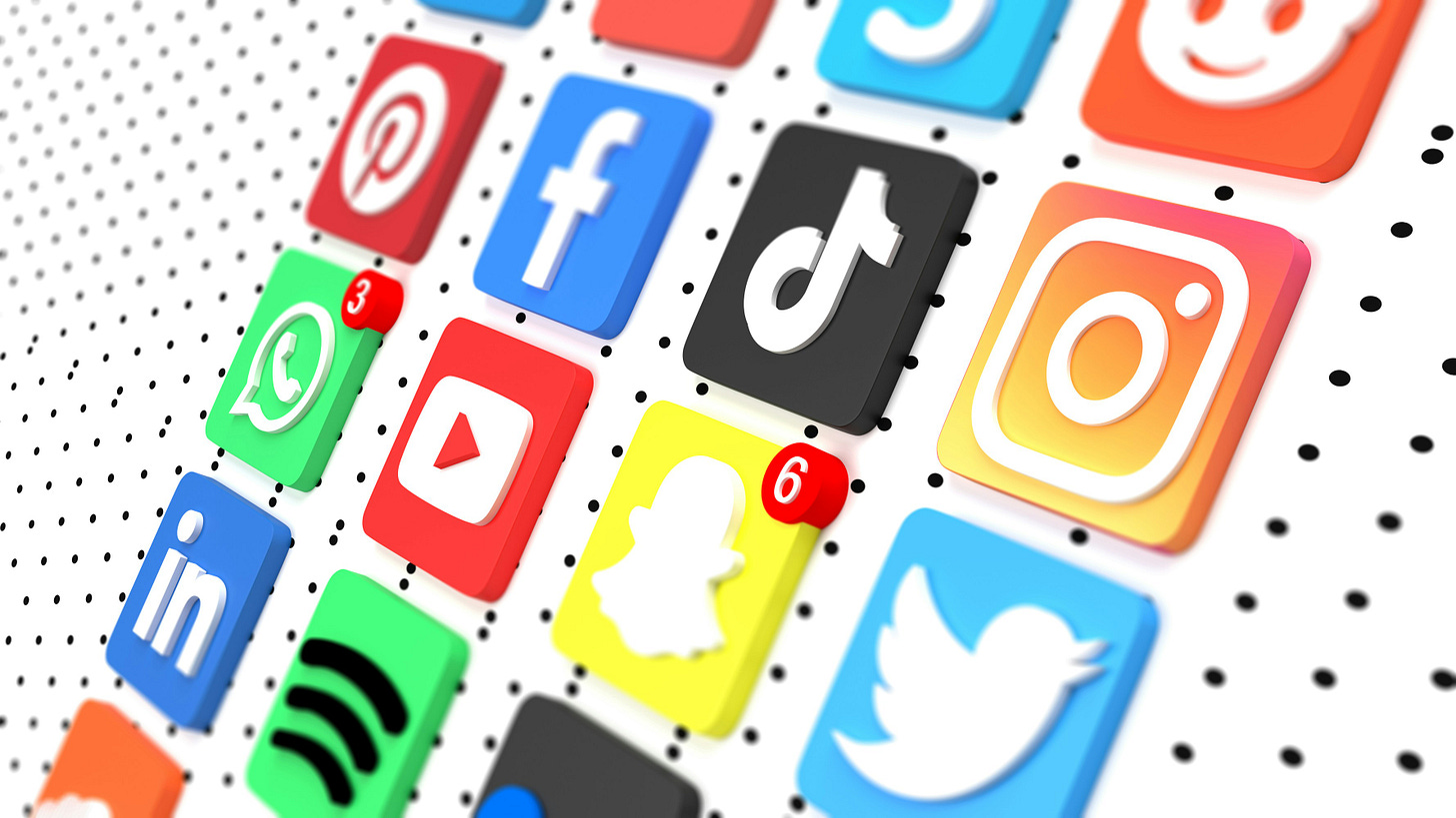 An angled, close-up shot of various 3D social media and digital platform icons arranged in a grid on a white surface with a black dotted pattern. Visible icons include TikTok, Instagram, Facebook, YouTube, WhatsApp, Pinterest, Snapchat, LinkedIn, and Twitter. Several icons feature red notification badges with numbers, and the shallow depth of field causes the icons in the background to appear blurred.