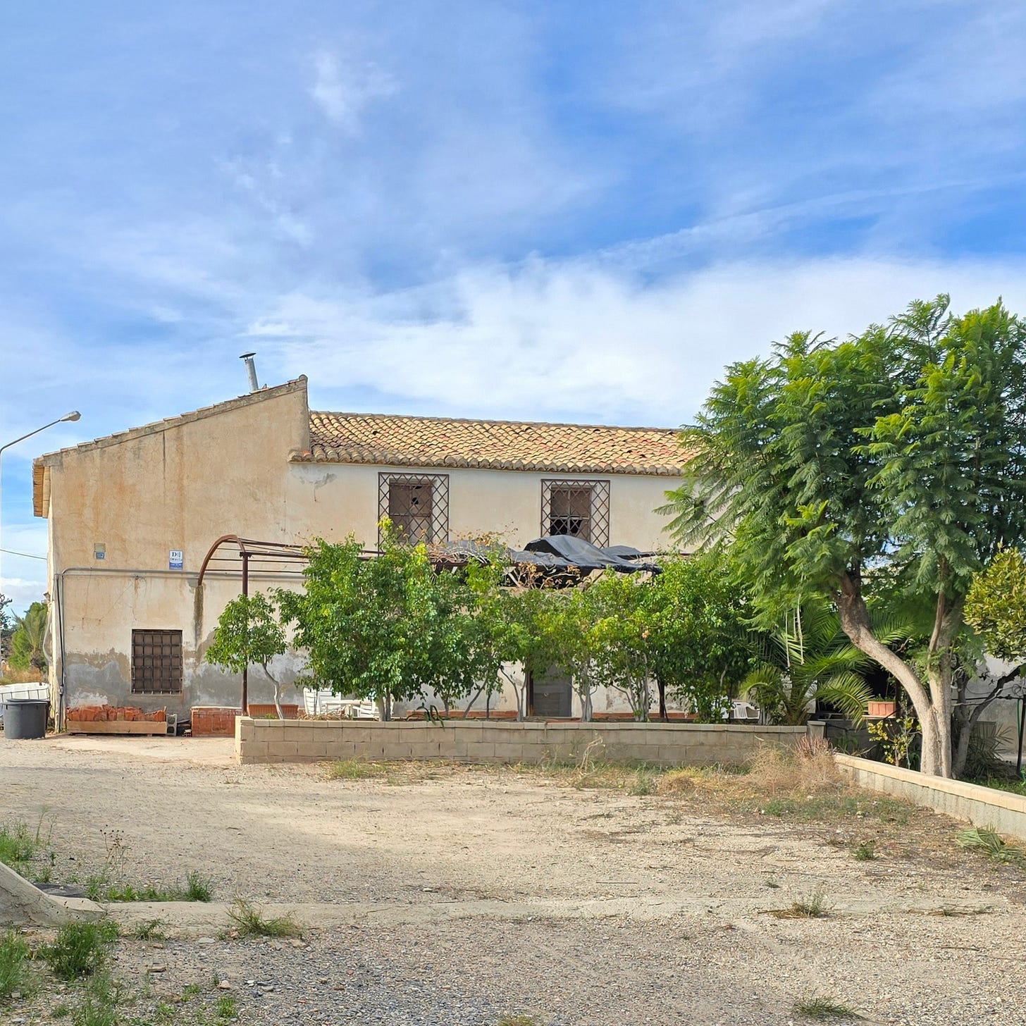 Rustic farmhouse in need of renovation in Spain. Trees outside. Blue skies