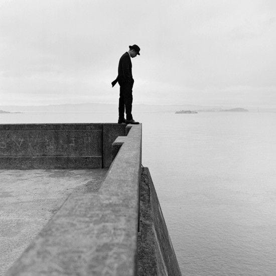 This may contain: a man standing on top of a cement wall next to the ocean in black and white This may contain: a man standing on top of a cement wall next to the ocean in black and white