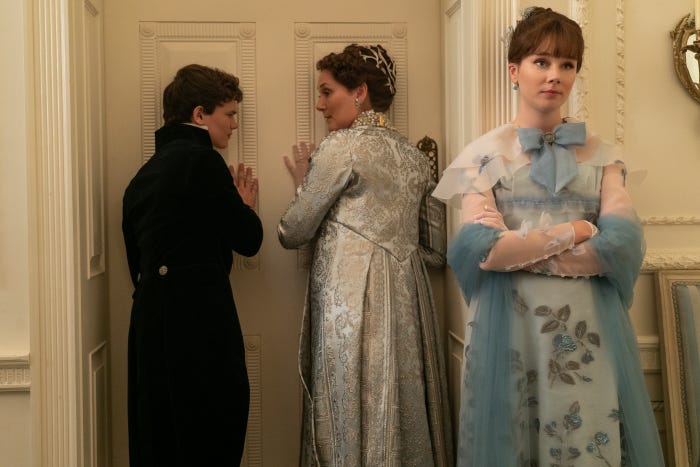 The Bridgerton family stand listening at a door. And Francesca Bridgerton plays a grand piano.