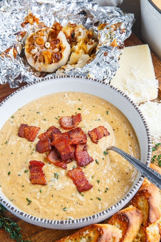 This may contain: a bowl of soup with bacon and cheese on the side next to some bread slices