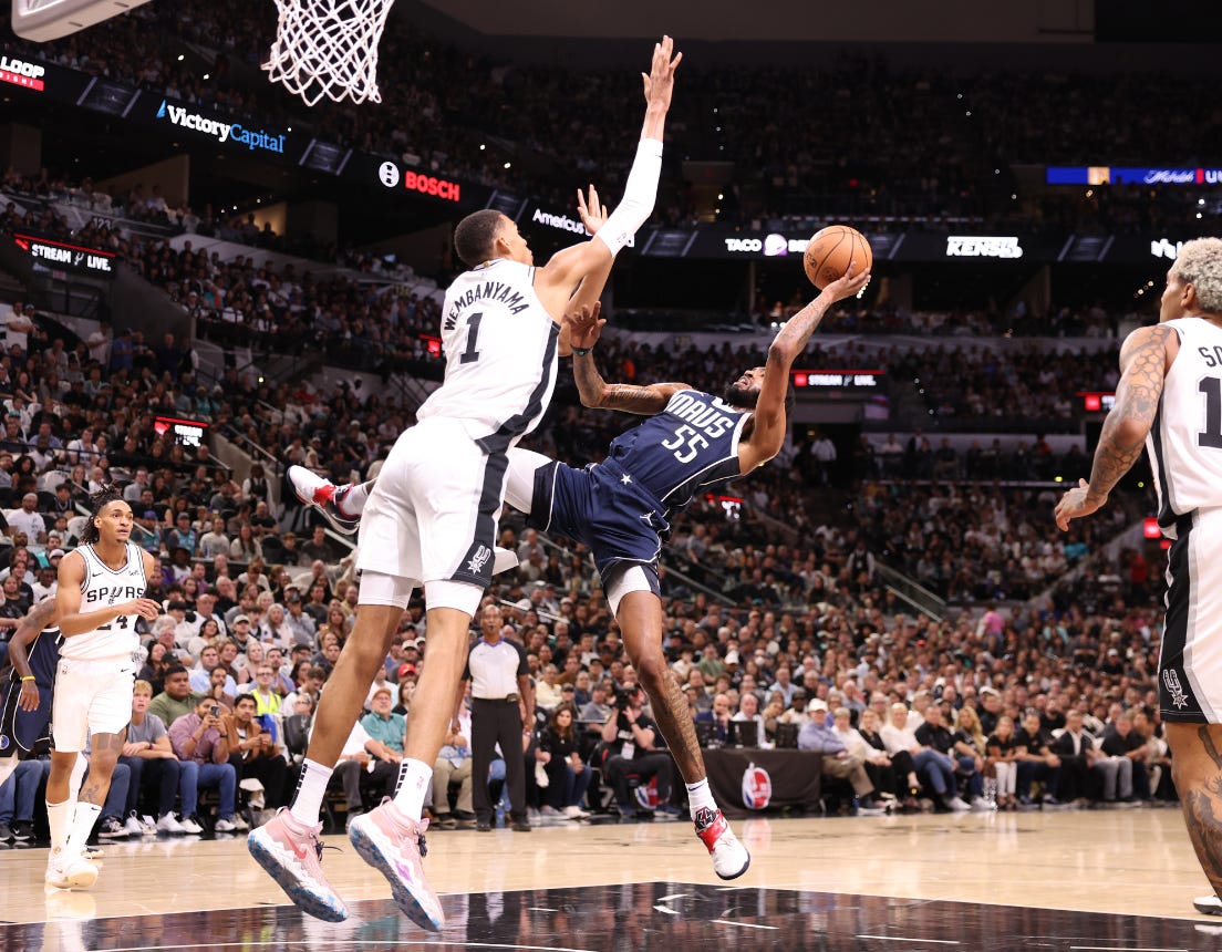 Defender challenges an acrobatic layup in a packed NBA arena during a fast-break.