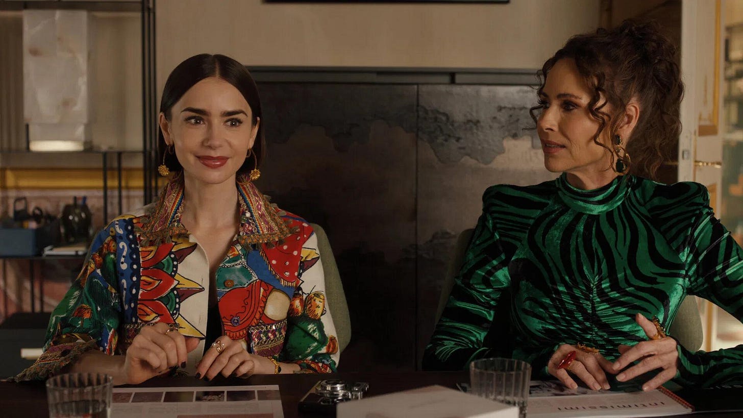 A scene from Emily In Paris Season 5 showing Emily Cooper sitting at a desk with Princess Jane