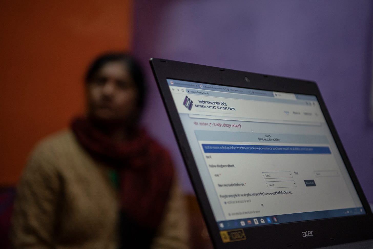 A laptop open with a website on the screen, in the backdrop of a waiting woman