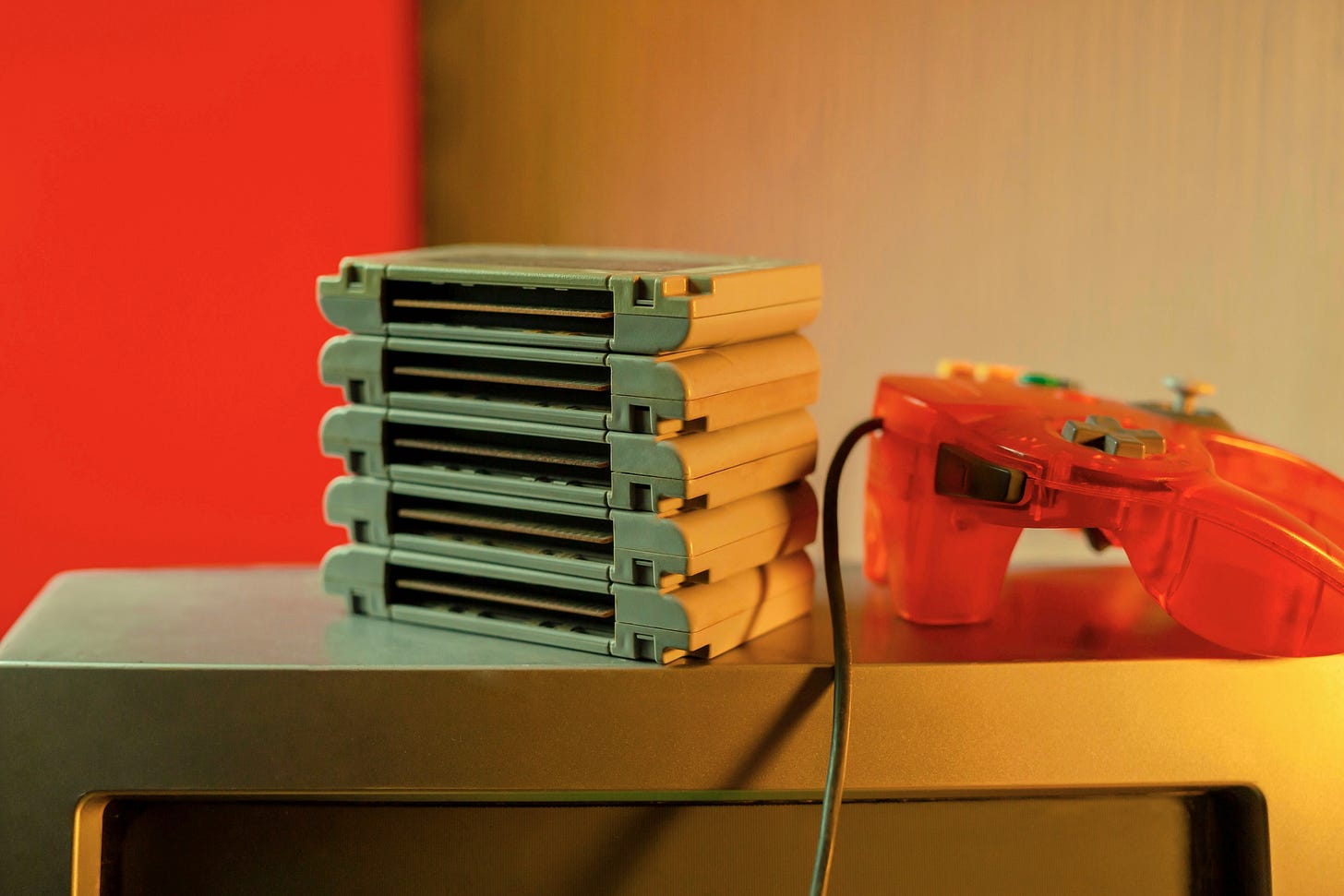 An orange controller on top of a CRT television beside a stack of catridges An orange controller on top of a CRT television beside a stack of catridges