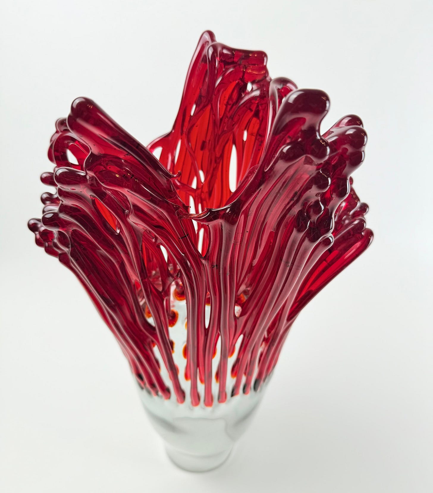 A red glass sculpture on white: ribbons of red glass rising and fanning out from a small clear base A red glass sculpture on white: ribbons of red glass rising and fanning out from a small clear base