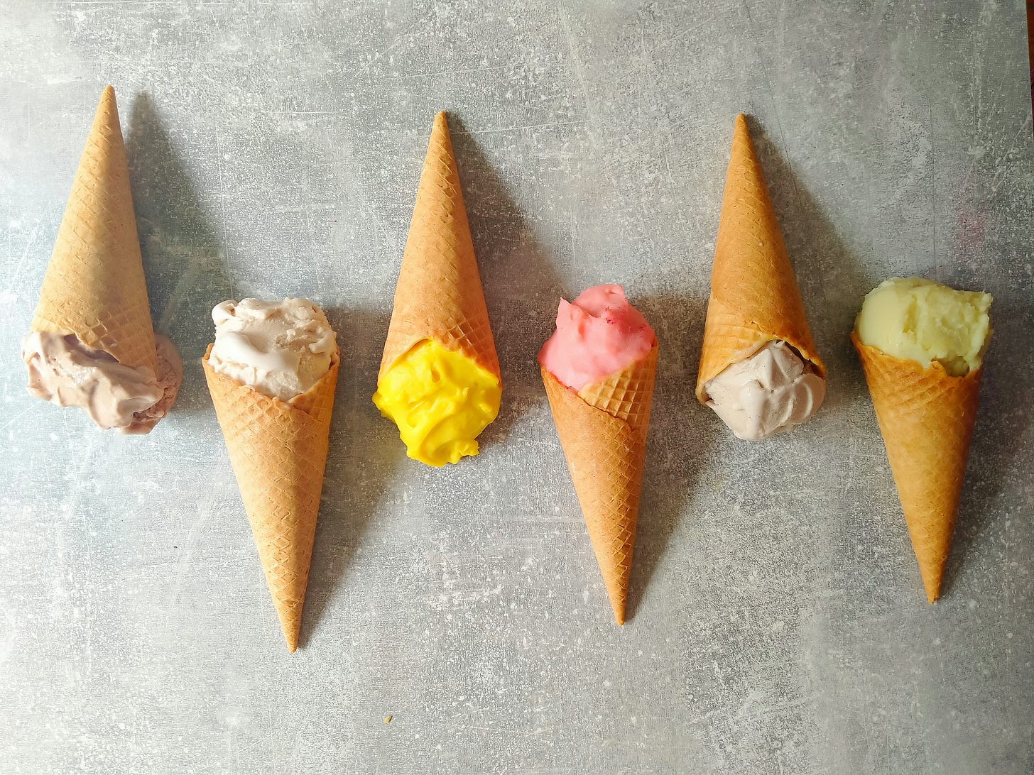 Six ice cream cones in various flavors lying on a flat surface.