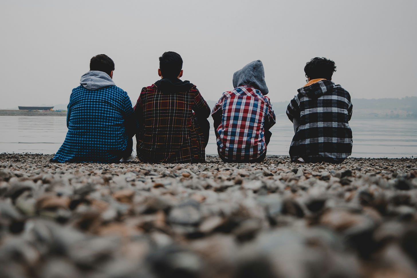 Four teens sitting on a beach facing away from the camera looking at the water.