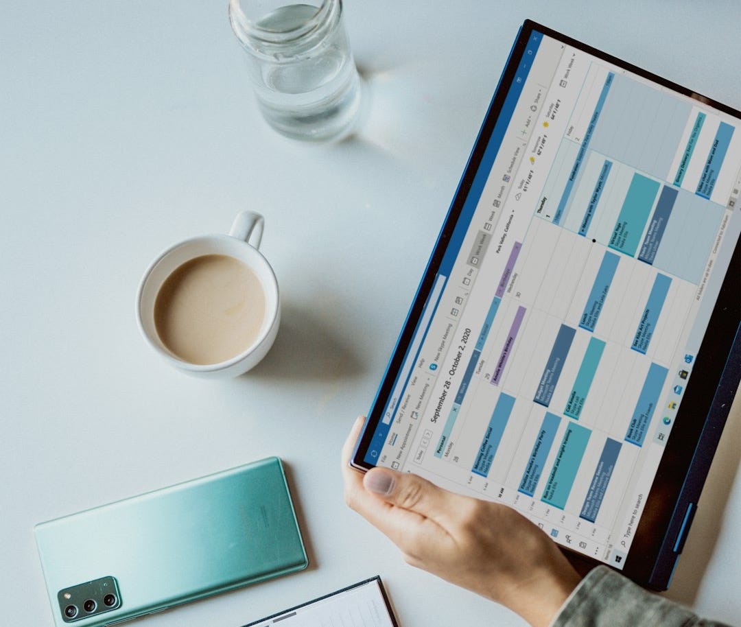 person holding ipad near white ceramic mug and laptop