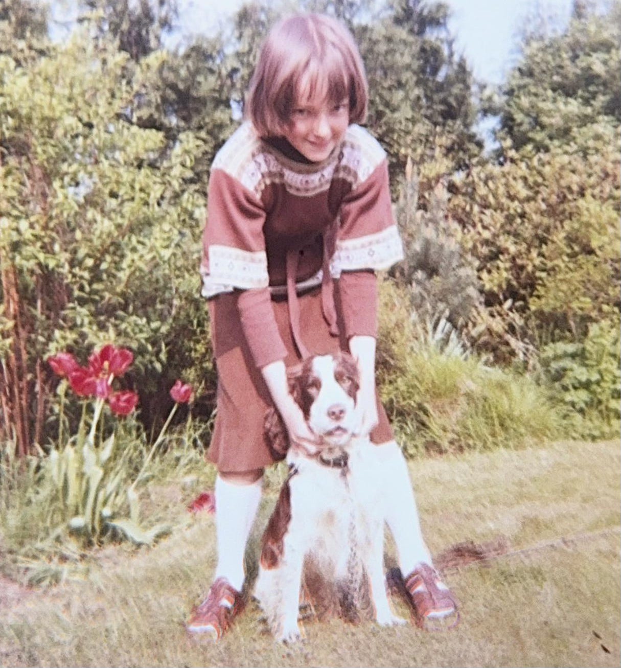 Jane, aged around 10, and cocker spaniel Jason in a green and flowery garden. Jane is standing behind Jason with her hands draped around him. Jane, aged around 10, and cocker spaniel Jason in a green and flowery garden. Jane is standing behind Jason with her hands draped around him.
