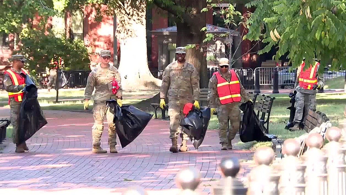 National Guard troops in uniform carry trash bags while cleaning Lafayette Park in Washington