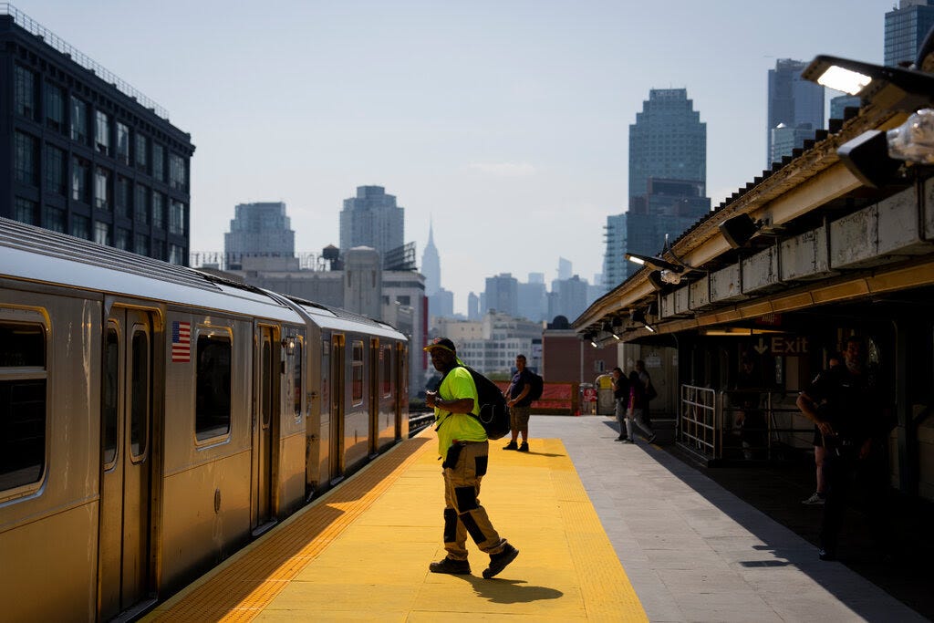A man in a neon yellow shirt stands on an outdoor subway platform.
