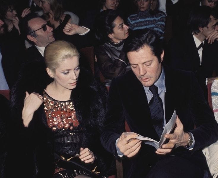 This may contain: a man and woman sitting next to each other in front of a group of people This may contain: a man and woman sitting next to each other in front of a group of people