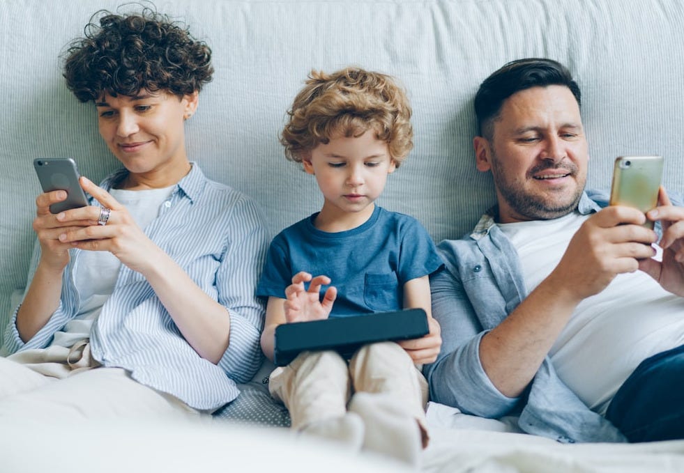 a man, woman and child sitting on a couch looking at their cell phones