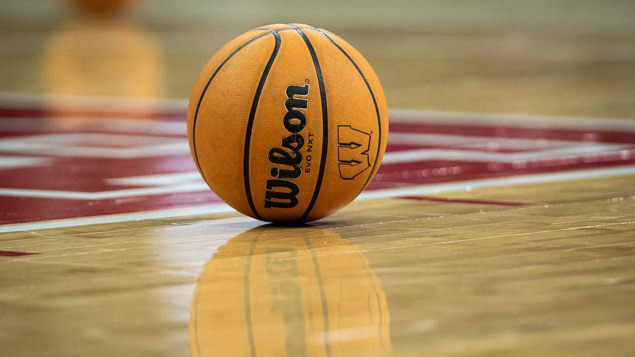 A Wilson basketball featuring the Wisconsin Badgers logo rests on the hardwood court at the Kohl Center.