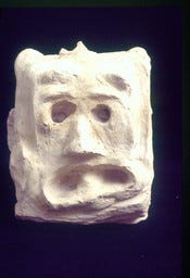A imagem 1 exibe uma escultura em busto de gesso ou material similar, que representa um guerreiro mitológico, uma obra do artista brasileiro Lúcio Noeman. A iluminação dramática com sombras profundas, destaca as características faciais angulares e expressivas da peça. O busto possui uma expressão séria e intensa, com sobrancelhas proeminentes e olhos fixos. O trabalho é notável pela sua qualidade artística e detalhes precisos, como a textura na parte de trás da cabeça, sugerindo um penteado ou adorno.  A imagem 2 A imagem mostra uma escultura de rosto em um material branco e áspero, que parece ser gesso ou pedra.  O rosto possui uma expressão contorcida, que transmite angústia, choque ou sofrimento, com olhos vazios e a boca aberta em um formato irregular. A textura da obra é rugosa e não polida, e a forma é aproximadamente retangular ou em bloco.