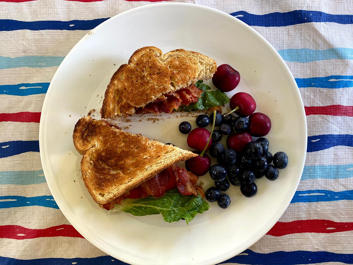 BLT Sandwich with fruit on white plate over red, white, & blue tablecloth