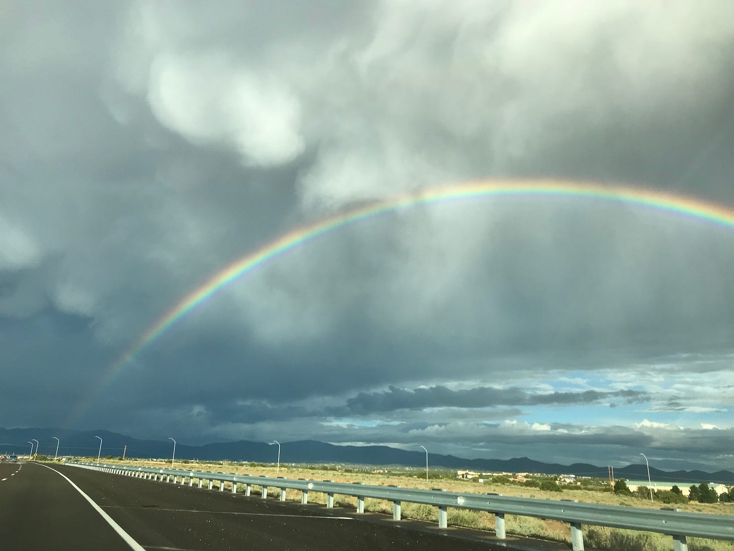 Arching rainbow in cloudy sky, seen from highway.