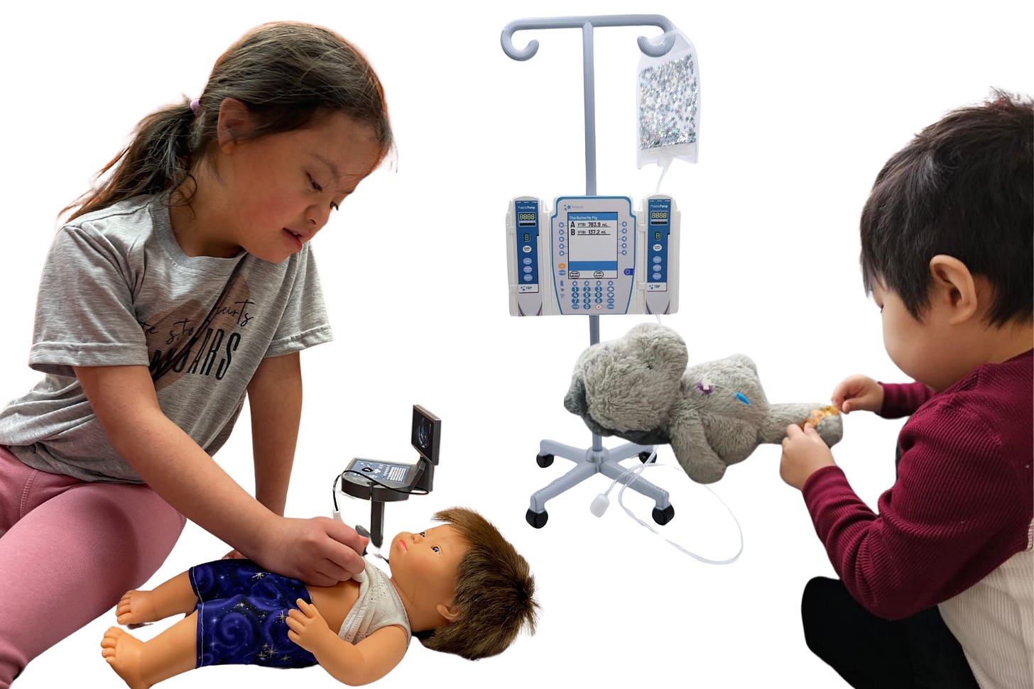 Two young children play with Butterfly Pig medical toys on a white background. A girl in a grey t-shirt and pink leggings leans over a doll using a miniature ultrasound machine, while a boy in a burgundy top adjusts the IV line on a grey stuffed elephant connected to a miniature double infusion pump on a drip stand with a glitter IV bag.