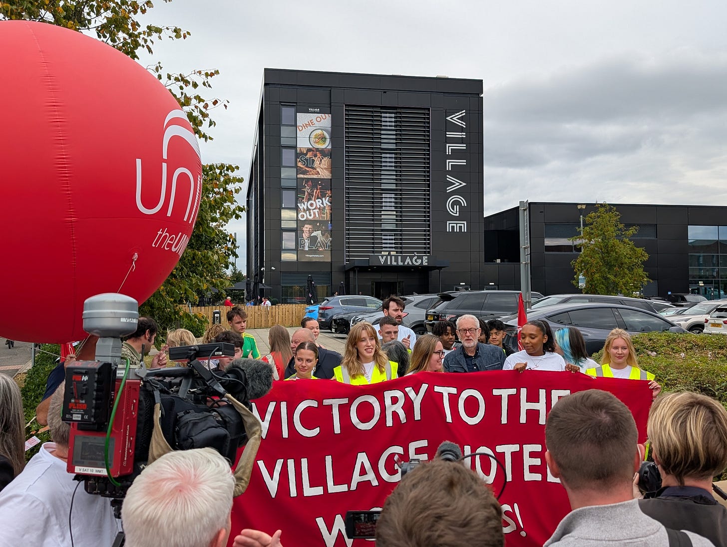 The picket outside the Village Hotel. Activists are stood behind a banner which reads "Victory to the Village Hotel Workers".