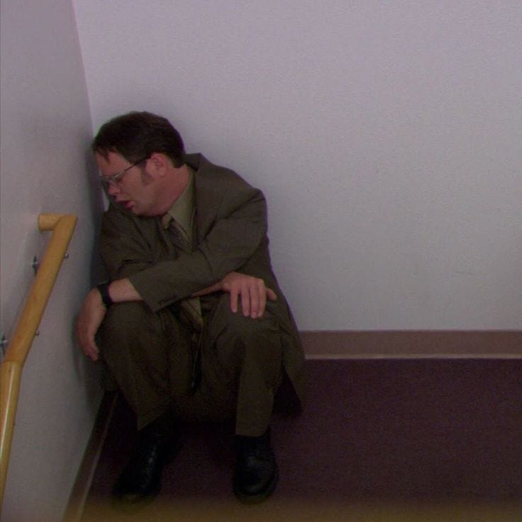 This may contain: a man sitting on the floor in front of a wall next to a toilet with his head down This may contain: a man sitting on the floor in front of a wall next to a toilet with his head down