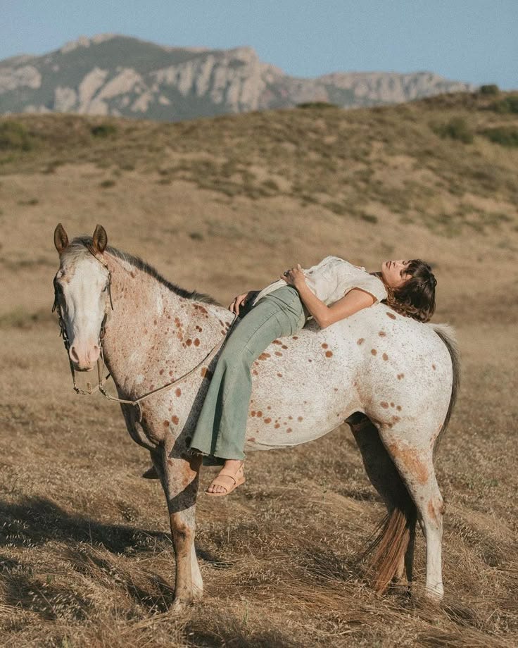 This may contain: a woman riding on the back of a brown and white horse in an open field